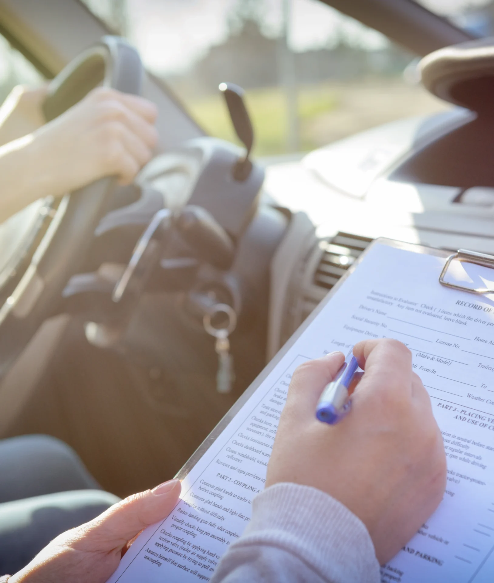 A person writing on paper in front of a car.